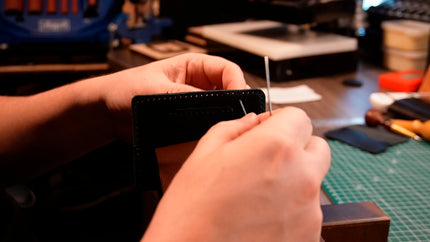 MZ Leather Craft atölyesinde bir zanaatkarın elleri; dikiş mengenesi (stitching pony) kullanarak siyah bir deri cüzdanı iki iğneyle elde dikerken geleneksel el dikişi (Saddle Stitch) aşaması.