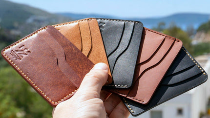 Bir elin fan şeklinde tuttuğu çeşitli Pueblo Kiremit, Natural, Siyah ve Buttero Kiremit, Siyah MZ Leather Craft minimalist deri kartlıklar. Bodrum manzarası eşliğinde el dikimi ve logolu kartlık çeşitlerinin görüntüsü.