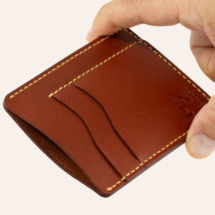 MZ Leather Craft dikey minimalist kiremit Buttero deri kartlık, el ile tutulan hafif açılı boş ön görünüm, kıvrımlı kart yuvaları ve sarı saraç dikişi detayları | The Vertical Minimalist Cardholder - Chestnut Buttero Leather by MZ Leather Craft, empty front view held by hand at a slight angle, showcasing curved card slots and yellow saddle-stitching details
