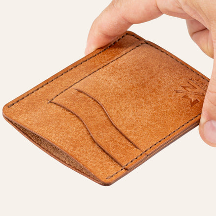 MZ Leather Craft dikey minimalist natürel Pueblo deri kartlık, el ile tutulan hafif açılı boş ön görünüm, kıvrımlı kart yuvaları ve kahverengi saraç dikişi detayları | The Vertical Minimalist Cardholder - Cognac Pueblo Leather by MZ Leather Craft, empty front view held by hand at a slight angle, showcasing curved card slots and brown saddle-stitching details